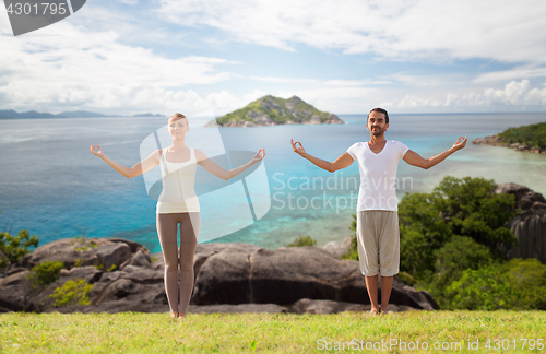 Image of happy couple making yoga exercises on beach