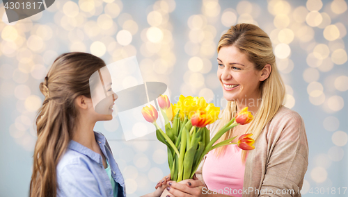 Image of happy girl giving flowers to mother over lights