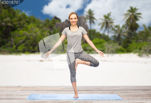 Image of woman doing yoga in tree pose on beach