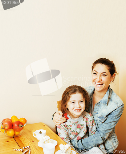 Image of young mother with daughter on kitchen drinking tea together hugging eating celebration cake on birthday party