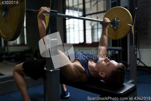 Image of young man flexing muscles with barbell in gym