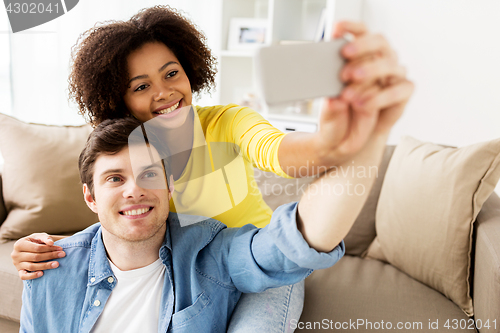 Image of happy couple with smartphone taking selfie at home