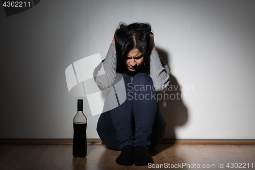 Image of woman with bottle of alcohol crying at home