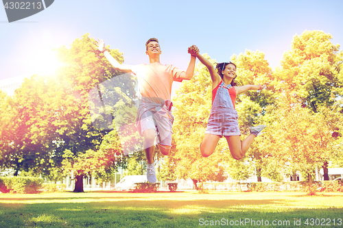 Image of happy teenage couple jumping at summer park