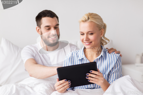 Image of smiling happy couple with tablet pc in bed at home