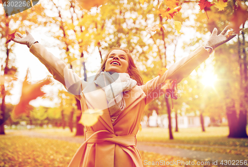 Image of happy woman having fun with leaves in autumn park