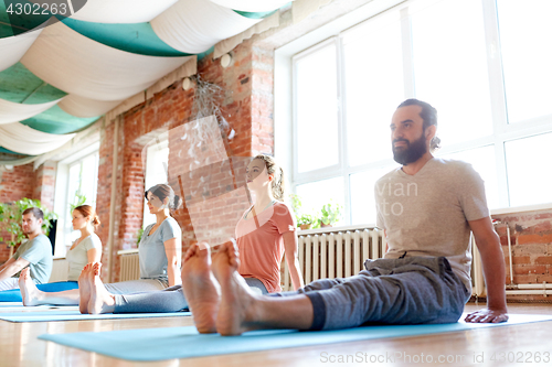 Image of group of people doing yoga staff pose at studio