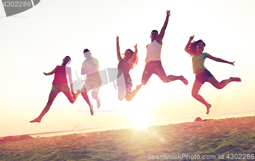 Image of smiling friends dancing and jumping on beach