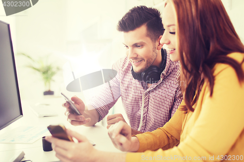 Image of happy creative team with smartphones at office