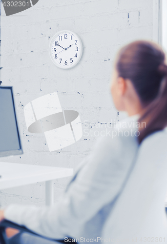 Image of businesswoman looking at wall clock in office