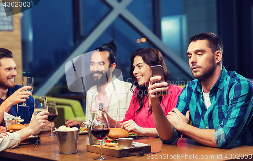 Image of man with smartphone and friends at restaurant
