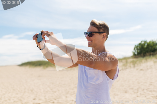 Image of man with smartphone photographing on summer beach