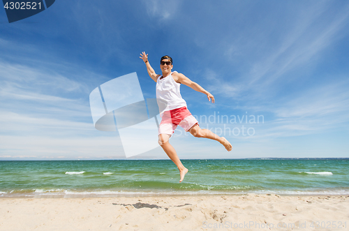 Image of smiling young man jumping on summer beach