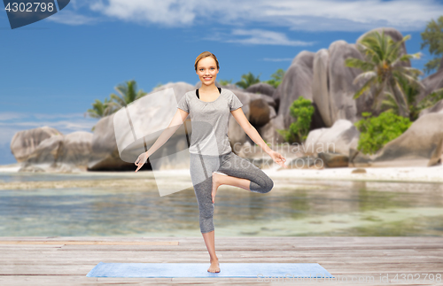 Image of woman doing yoga in tree pose on beach