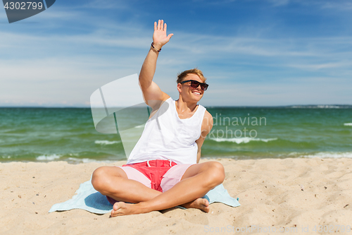 Image of happy smiling young man sunbathing on beach towel