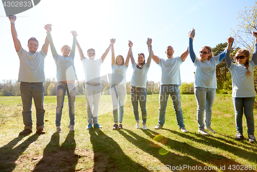 Image of group of happy volunteers holding hands outdoors