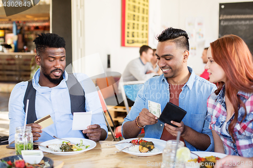 Image of happy friends paying bill for food at restaurant