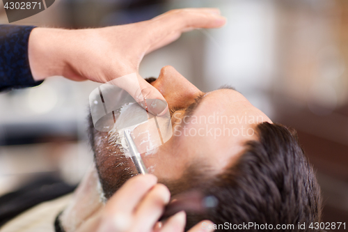 Image of man and barber with straight razor shaving beard