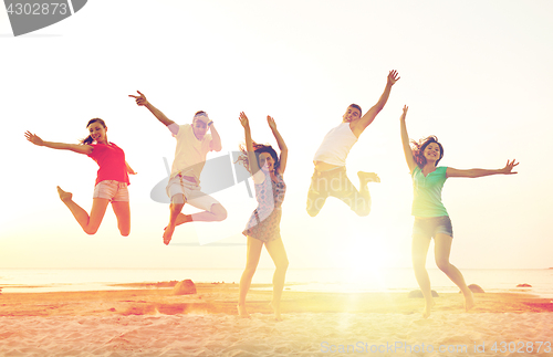 Image of smiling friends dancing and jumping on beach