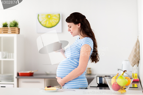Image of happy pregnant woman with mug and cake at home