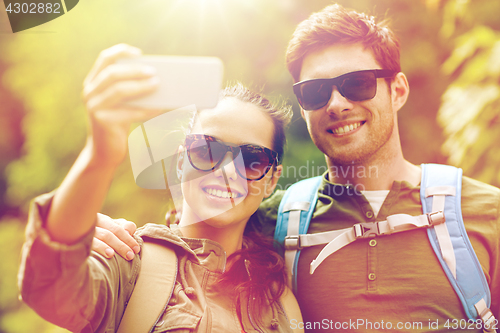 Image of couple with backpacks taking selfie by smartphone