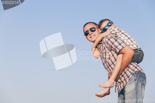 Image of Dad and son in sunglasses playing in the park at the day time.