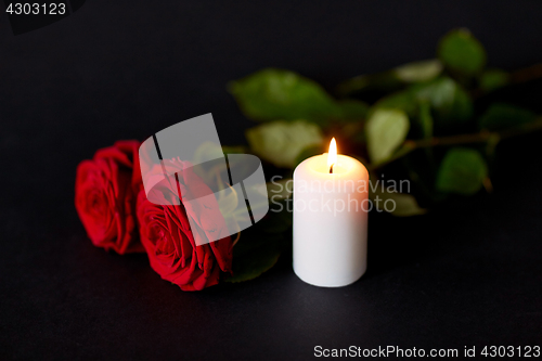 Image of red roses and burning candle over black background