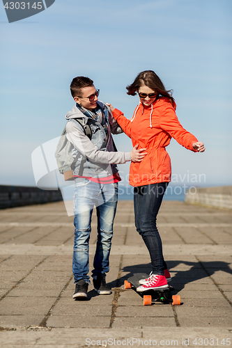Image of happy couple with longboard riding outdoors