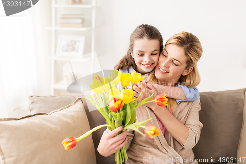 Image of happy girl giving flowers to mother at home