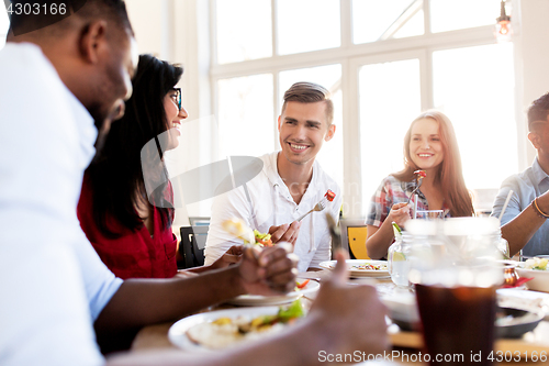 Image of happy friends eating and talking at restaurant