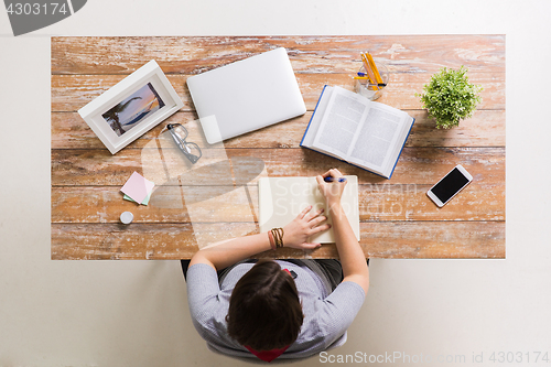 Image of woman with book writing to notebook at table