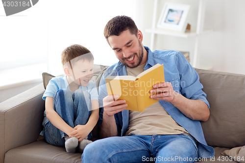 Image of happy father and son reading book sofa at home