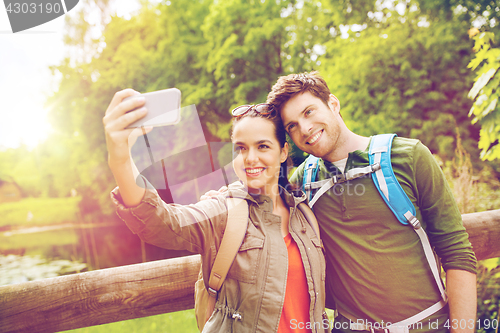 Image of couple with backpacks taking selfie by smartphone