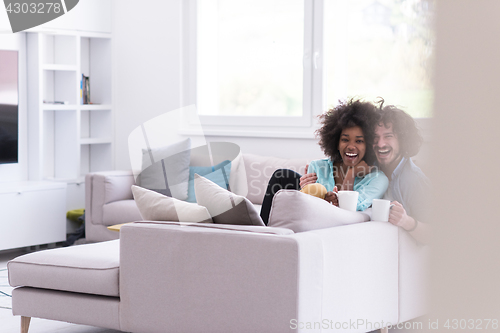 Image of multiethnic couple sitting on sofa at home drinking coffe