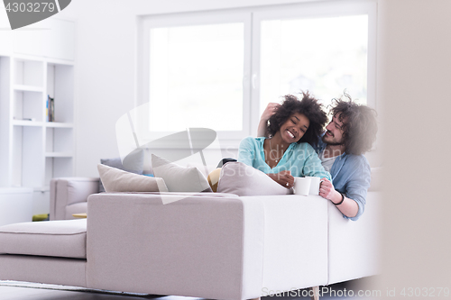 Image of multiethnic couple sitting on sofa at home drinking coffe