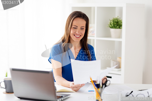 Image of happy woman with papers and laptop at office