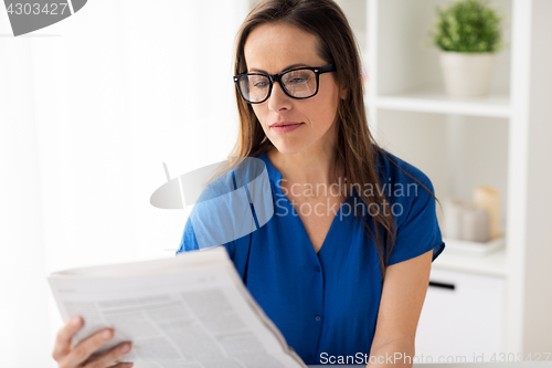 Image of woman in glasses reading newspaper at office