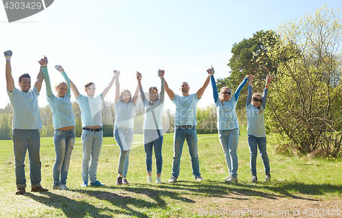 Image of group of happy volunteers holding hands outdoors