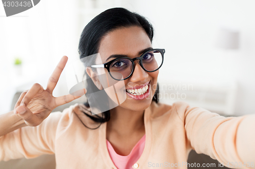 Image of smiling woman taking selfie and showing v sign