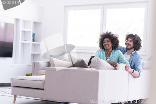 Image of multiethnic couple sitting on sofa at home drinking coffe