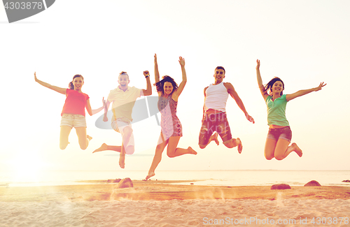 Image of smiling friends dancing and jumping on beach