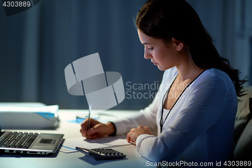 Image of woman with calculator and papers at night office