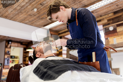 Image of man and barber with trimmer cutting beard at salon