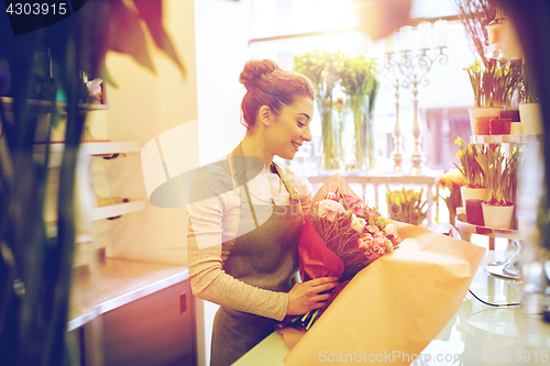Image of smiling florist woman packing bunch at flower shop
