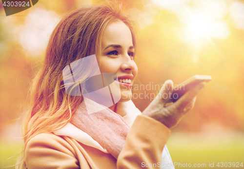 Image of woman recording voice on smartphone in autumn park