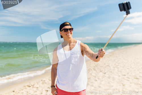 Image of man with smartphone selfie stick on summer beach