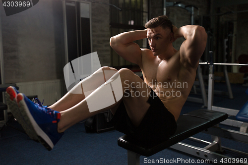 Image of young man doing sit-up abdominal exercises in gym