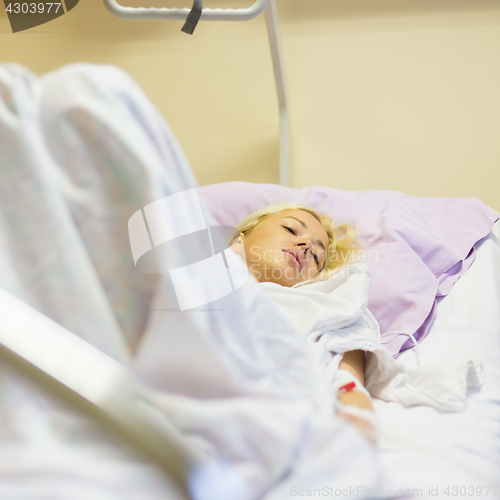 Image of Bedridden female patient recovering after surgery in hospital care.