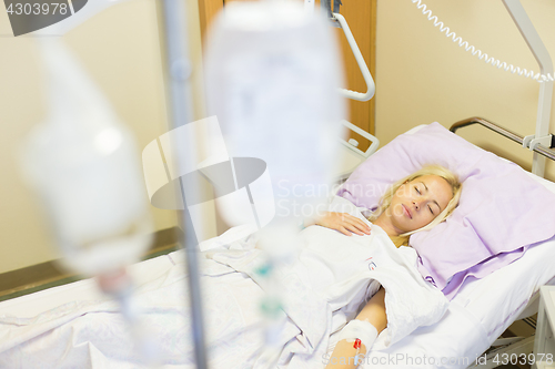 Image of Bedridden female patient recovering after surgery in hospital care.