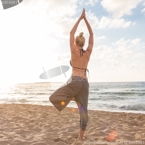 Image of Woman practicing yoga on sea beach at sunset.